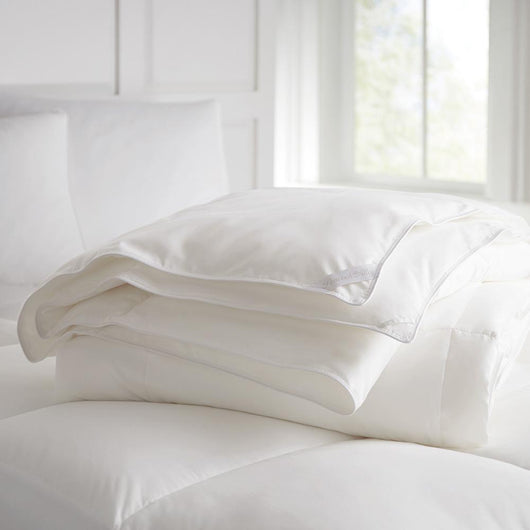 White goose down duvet folded laying on a bed with mattress enhancer